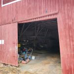 Punainen ulkorakennus, avonainen liukuovi ja näkyvissä pihatyövälineitä