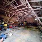 Ulkorakennuksen sisätila, näkyvissä kattotuoleja, työkaluhyllyjä ja varastotavaraa