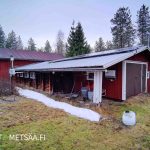 Punainen piharakennus, katolla aurinkopaneelit ja näkyvissä ulkoyksiköt