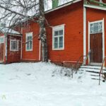 Punaisen koulurakennuksen sisäänkäynti ja puiset rappuset lumen keskellä.