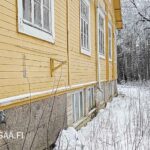 Keltaisen puukoulun julkisivua ja luonnonkivijalkaa talvisessa maisemassa.