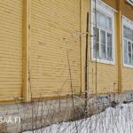 Keltaisen puukoulun julkisivua ja luonnonkivijalkaa talvisessa maisemassa.