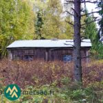 Vanha puurakennus puiden ja kasvillisuuden ympäröimänä.